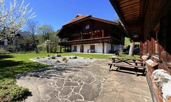 A traditional wooden house with a balcony surrounded by a green meadow. The clear blue sky creates an idyllic atmosphere.