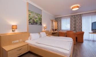 A modern hotel room with a double bed and a large window. The furnishings include a seating area and a cozy atmosphere.