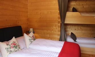 A cozy wooden room with a double bed and a bunk bed. The walls are made of wood, and there is a pleasant, warm atmosphere.