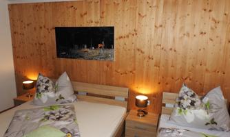 A cozy bedroom with wood paneling, two beds, and soft lighting. A picture of a forest hangs on the wall.