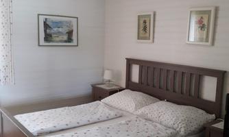 A cozy bedroom with a double bed and fresh bed linens. There are some pictures hanging on the walls, and there is a bedside table next to the bed.