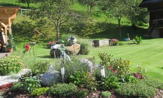 A beautiful garden with colorful flowers and green plants. In the background, there are some decorative stones and a well-maintained lawn.
