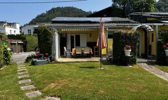 A beautiful property with a garden and a terrace. In the background, green hills and a blue sky can be seen.