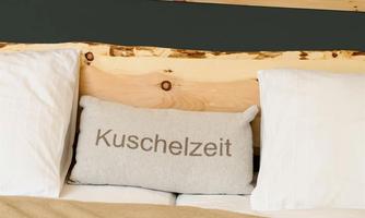 A cozy bed with white pillows and a gray pillow that says "Cuddle Time." The wooden paneling in the background adds a warm atmosphere.