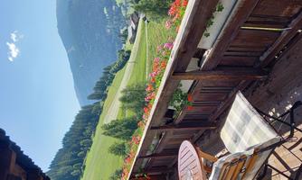 A beautiful balcony with a table and chairs. The view shows green hills and forests under a blue sky.