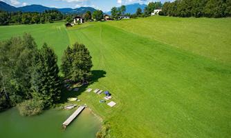 A picturesque landscape with a green meadow and a small pond. In the background, there are some houses and trees visible.