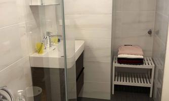 A modern bathroom with a shower and a sink. Towels and toiletries are placed on a shelf.