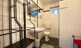 A modern bathroom with white tiles and a dark floor. It includes a sink, a toilet, and a shower.