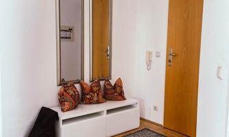 A bright and inviting entrance with a carpet and a seating area. Two mirrors hang on the wall, and a door leads outside.