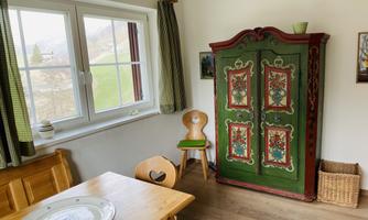A cozy room with a traditional green cupboard and a wooden table. Through the window, you can see the green landscape outside.