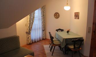 A cozy living space with a dining area and a sofa. Bright walls and a window provide an inviting atmosphere.
