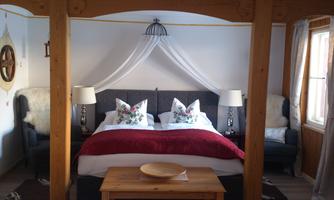 A cozy bedroom with a large bed and decorative pillows. Next to the bed are two armchairs and stylish lamps.