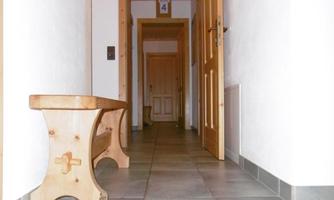 A bright hallway with gray tiles and wooden-clad doors. On the left side, there is a simple wooden bench.