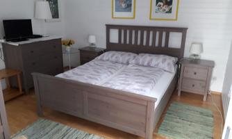A cozy bedroom with a large gray bed and wooden floor. The room is decorated with artwork and has a television.