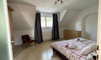 A bright bedroom with a large bed. Windows with curtains and light walls create a pleasant atmosphere.