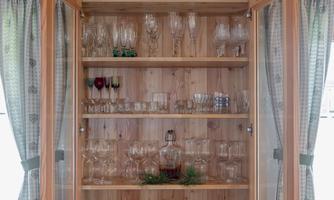 A wooden cabinet with glasses and plates. The glasses are neatly stacked, and the cabinet has large glass doors.
