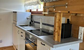 A modern kitchen with wood paneling and a gray work area. It is well equipped with a sink, stove, and shelves for cups.