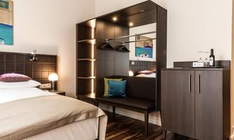 A modern hotel room with a large bed and stylish furniture. The room is well-lit and offers a cozy atmosphere.