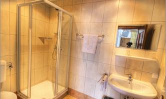A bright bathroom with a shower and a sink. The walls are tiled and there is a mirror above the sink.