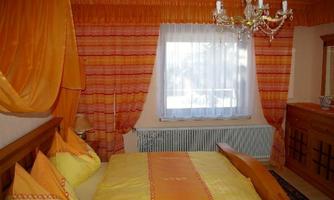 A cozy bedroom with orange curtains and bedding. The room has a window with plenty of light and an elegant ceiling lamp.