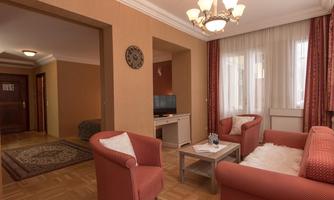 A cozy living room with red sofas and a table. Outside, there is plenty of daylight coming through large windows.
