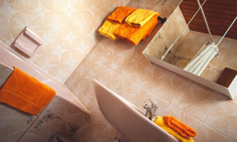 A bathroom with tile patterns and bright orange towels. A sink and a mirror are visible.