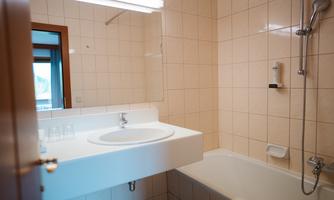A modern bathroom with a bathtub and a sink. The walls are tiled in light colors and a mirror hangs above the sink.