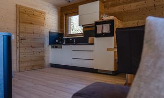 A modern kitchen in a wooden house with a large window. The floor is made of light wood, and the furnishings are functional and stylish.