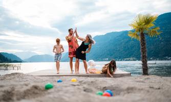 A cheerful family at the beach with a beautiful view of the lake. Children are playing in the sand while the adults are enjoying themselves and interacting with each other.