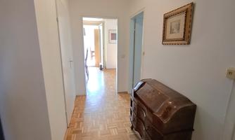 A bright hallway with parquet flooring and an old dresser. At the end of the hallway, several doors are visible.