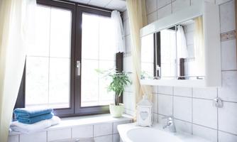 A bright bathroom with a large window and pleasant decoration. On the windowsill, there are potted plants and colorful towels are neatly folded.