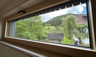 A large window with a view of green meadows and hills. In the background, trees and a small house can be seen.