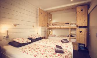 A cozy room with a double bed and a wooden bunk bed. The bedding has a floral pattern and the walls are made of light wood.