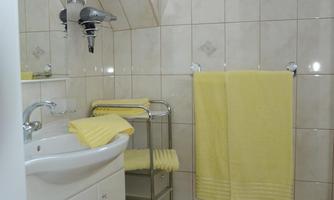 A bright bathroom with tiles and two windows. Yellow towels and a sink are clearly visible.
