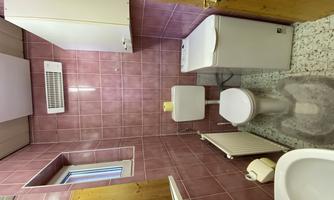A small bathroom with pink tiles. It contains a toilet, a sink, and a washing machine.