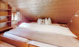 A cozy bedroom in the attic with wooden paneling. There is a large bed and a shelf for personal items.