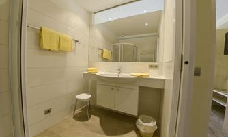 A modern bathroom with bright tiles and plenty of space. It has a shower, a sink, and yellow towels.