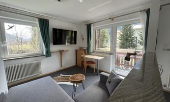 A bright living room with a gray sofa and a table. Large windows offer a view of the nature outside.