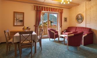 A cozy living room with red sofas and a dining table. Large windows offer views of nature.