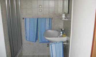 A modern bathroom with a shower corner and sink. Two blue towels hang on the wall.