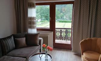 A cozy living space with a sofa and an armchair. Large windows provide a view of the green landscape outside.