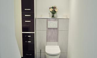 A modern bathroom with a white toilet and a simple sink. A narrow cabinet stands on the wall, and a small bouquet of flowers decorates the room.