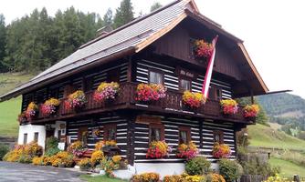 A traditional wooden house with colorful flower boxes and a beautiful garden. In the background, gentle hills and trees are visible.