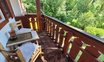 A cozy balcony with two wooden chairs and a small table. The view shows a green, wooded landscape.
