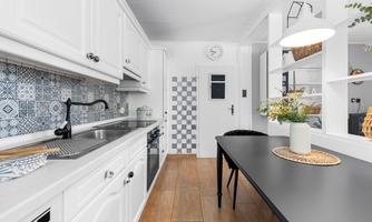 A modern kitchen with white cabinets and a tile design in shades of blue and gray. A black dining table with a decorative flower vase is located in the room.
