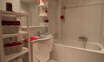 A modern bathroom with a bathtub and a shower. The walls are covered with white tiles, and there are shelves with towels and toiletries.