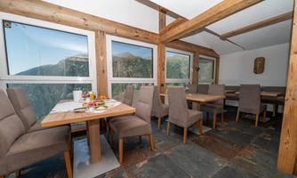 A modern restaurant with wooden decor and cozy tables. Through large windows, there is a view of the surrounding mountains.