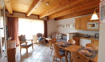 A bright and inviting kitchen with a dining area. The wooden beam ceiling and cozy furnishings create a warm atmosphere.