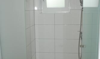 A modern bathroom with a newly designed shower. The walls are tiled with light tiles and there is a small window.