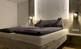 A modern bed in a cozy room with wooden details. The pillows are purple and the room is softly lit.